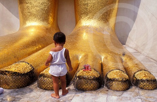 Photo of kid at the feet of a Buddha in Thailand